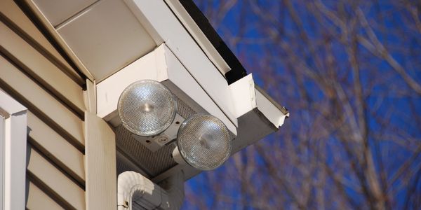 Outdoor security lights mounted on a house corner against a clear blue sky.