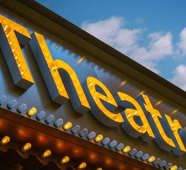 Close-up of a glowing theatre sign with lights against a blue sky.