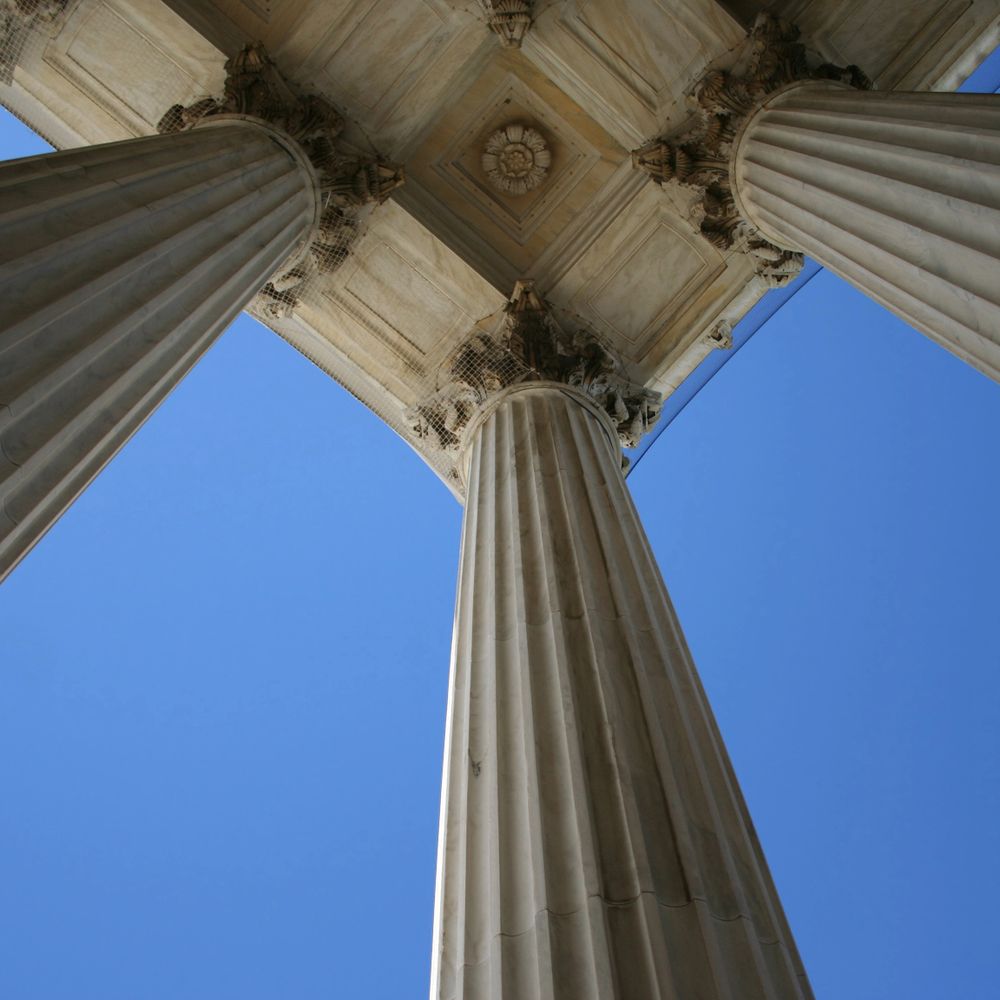 Looking up at three classical marble columns against a clear blue sky.