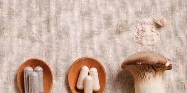 Wooden spoons with capsules beside a king oyster mushroom on a fabric surface.