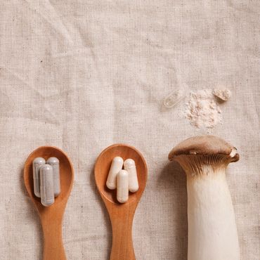 Two wooden spoons with mushroom capsules beside a fresh mushroom.