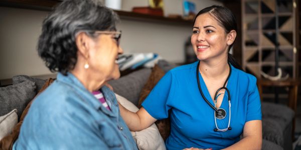 Nurse smiling and comforting elderly woman at home.