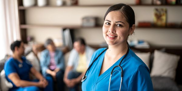 Smiling nurse in blue scrubs with stethoscope in a home setting.