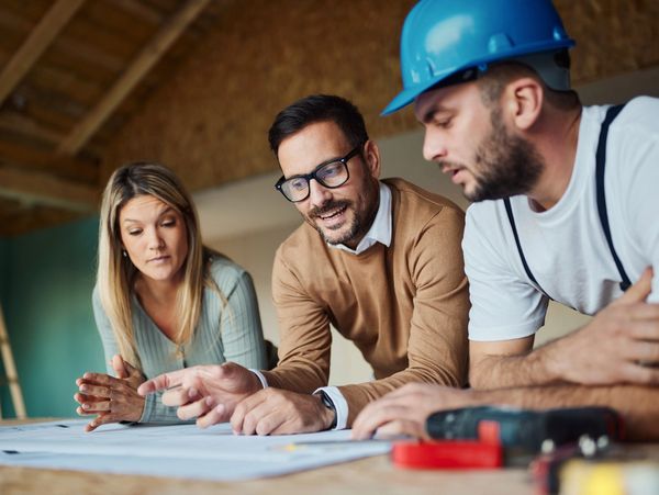 Three professionals review blueprints, including a man with a blue hard hat.
