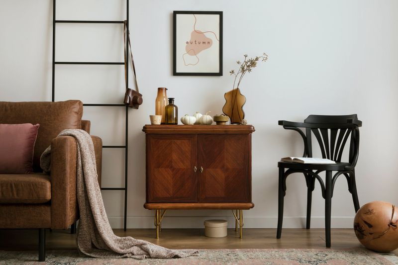 Warm and cozy living room interior with mock up poster frame with vintage sideboard, black chair, vase with dried flowers, box, carpet, pumpkins, sofa and personal accessories. Home decor. Template.