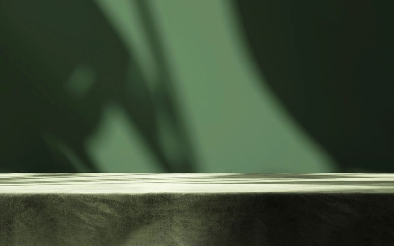 Table countertop with dark green velvet tablecloth in sunlight, tropical leaf shadow on blank wall in background for luxury food, beverage, nature, organic beauty cosmetic, fashion product display