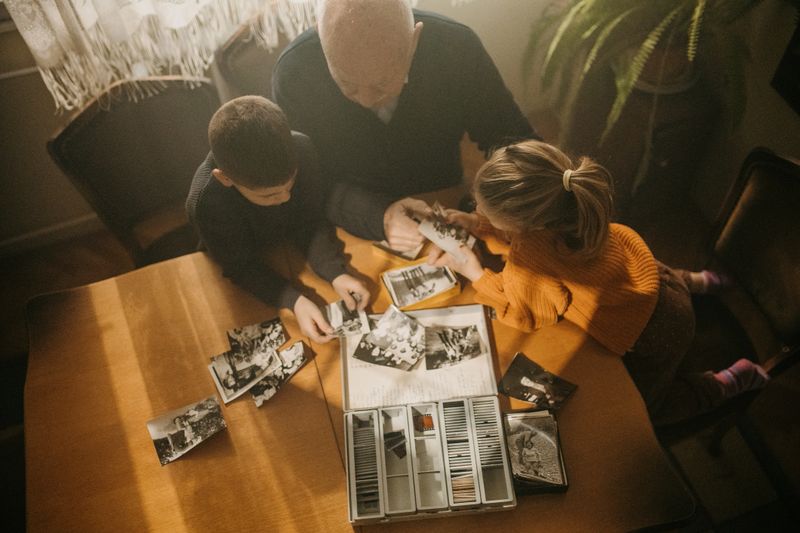 Grandfather with grandson and granddaughter sitting at the table and looking at photographic slides at grandpa's home.