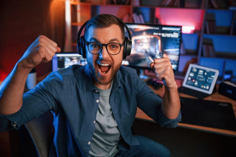 Uplifting and energized man is playing the shooter game on his computer. Neon lighting.