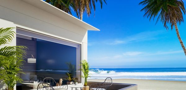 Modern beach house patio with ocean view and palm trees.