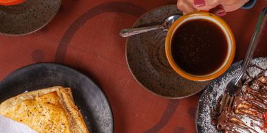 A cup of coffee with pastries on plates on a brown table.