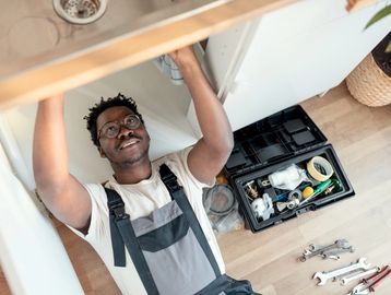 Man fixing sink plumbing with tools spread on floor.