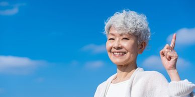 Smiling elderly woman pointing upwards against a blue sky.