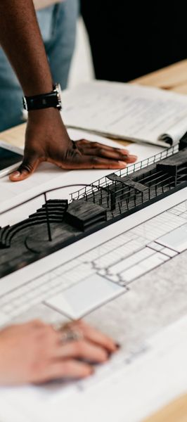 Hands examining an architectural model and blueprints on a table.
