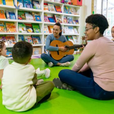 Teacher playing guitar for children in a colorful library setting.