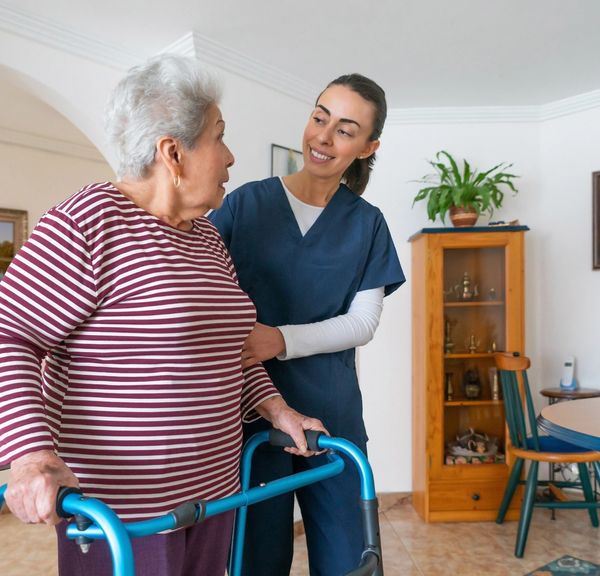 Caregiver assisting elderly woman using a walker.