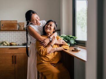 Young woman hugging elderly woman in a kitchen.