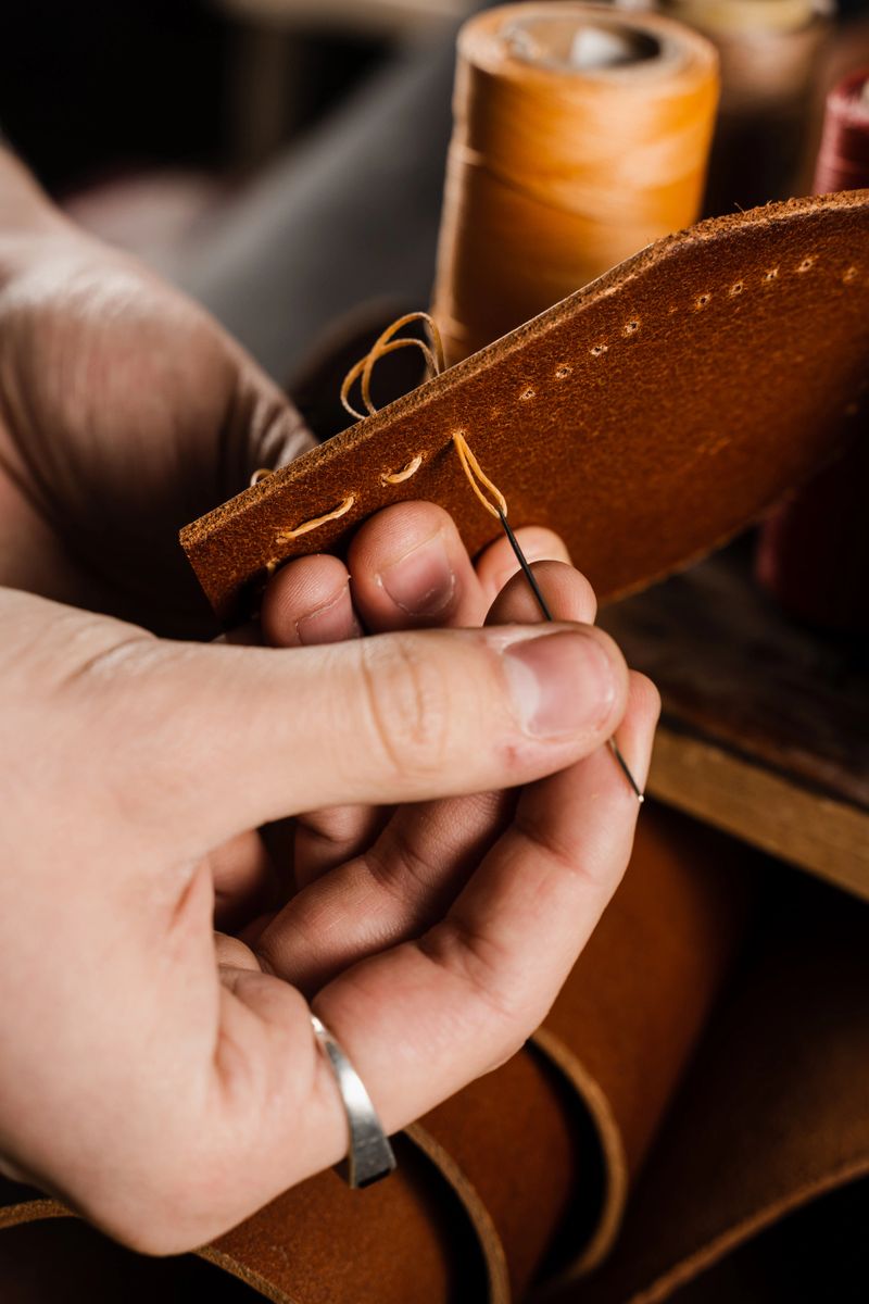 Craftsman sews genuine leather using needle and thread for creation natural leather products. Equipment for genuine leather production in workshop. Process of stitching genuine leather