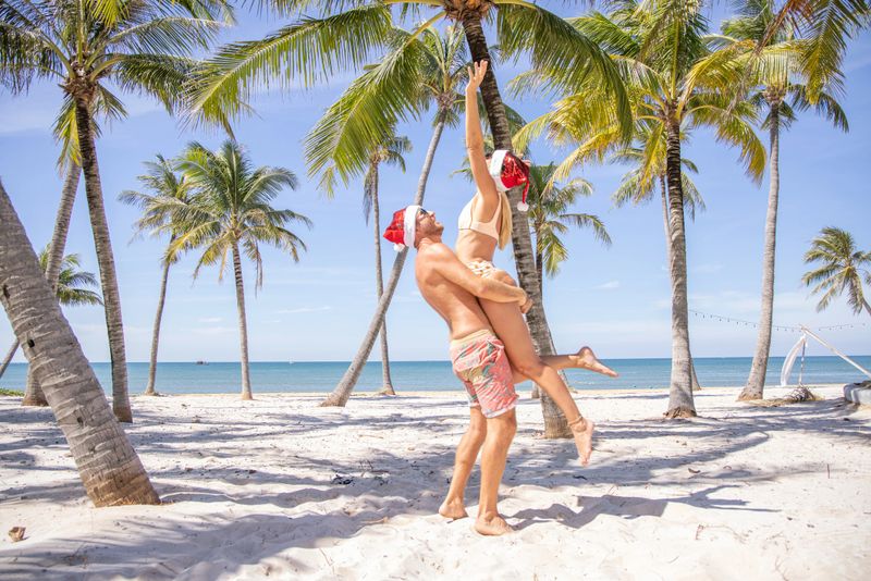 December, resort settings, palm tree Christmas vacation celebration by the beach. Couple wears Santa hat, happy moments, palm tre settings