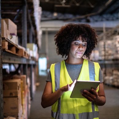 Warehouse worker in a reflective vest using a tablet for inventory management.