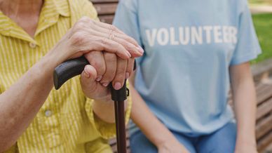 Volunteer holding an elderly person's hand on a walking cane, showing care and support.