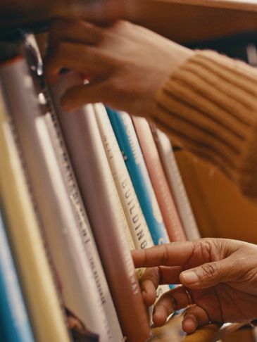 A person selecting a book from a bookshelf with a cozy sweater sleeve.