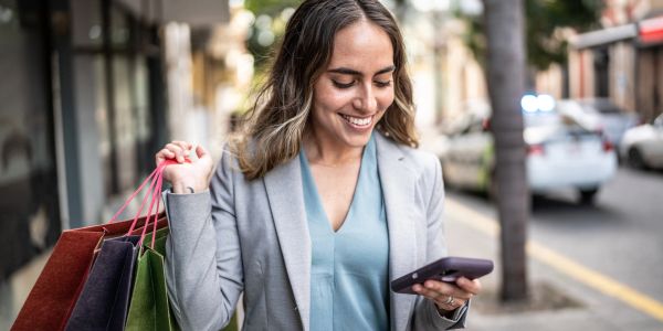 Happy woman holding shopping bags and looking at her phone on the street.