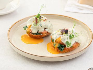 Eggs Benedict with creamy sauce and greens on a plate.