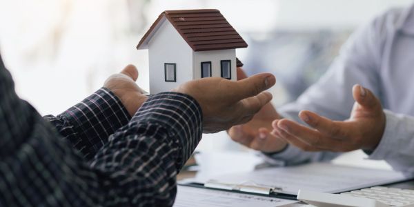 Person holding a miniature house model during a discussion.