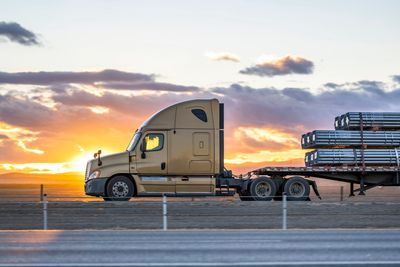 Gold tractor trailer with a flatbed trailer parked. Commercial driver with sunset behind