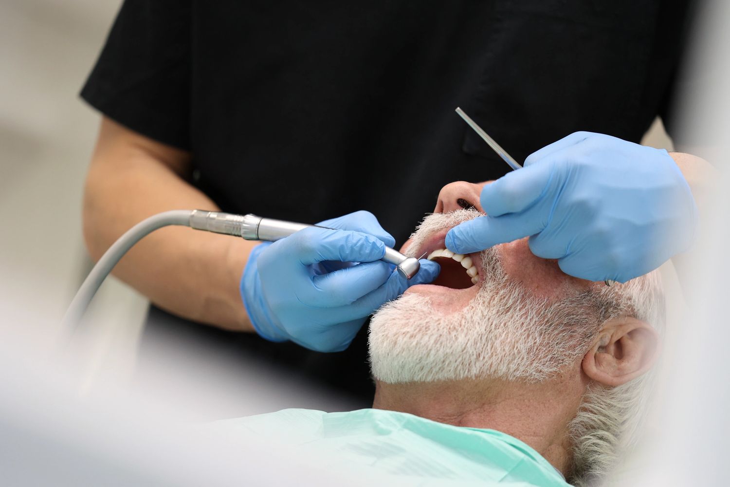 Dentist treating an elderly man with dental tools.
