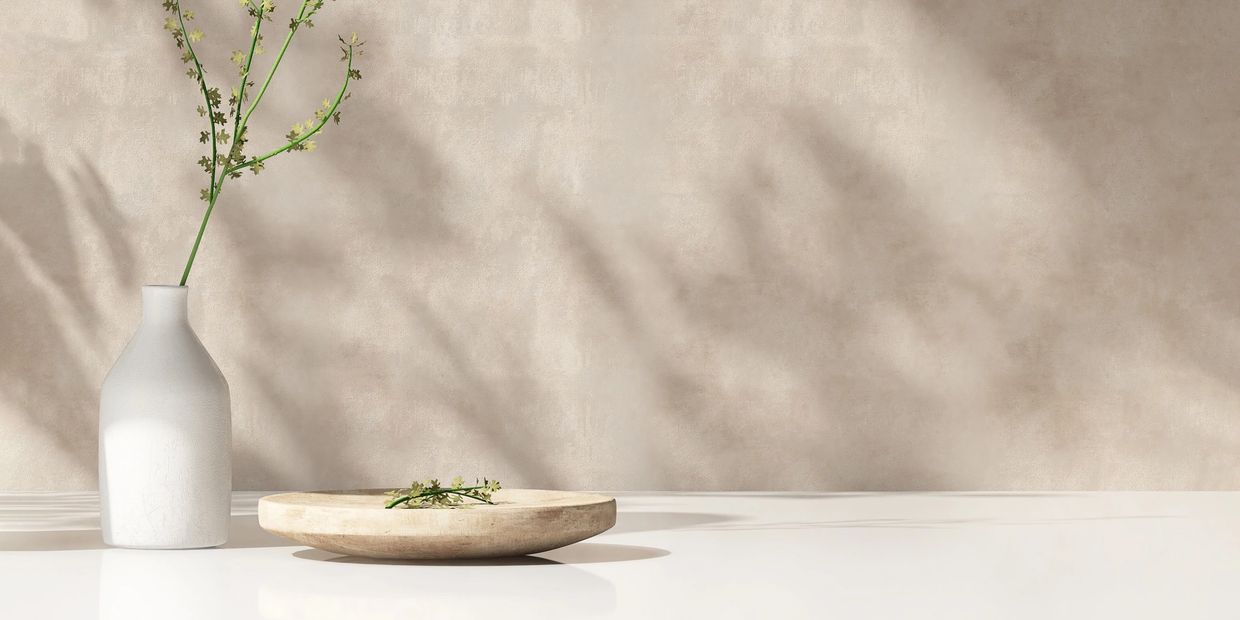 Minimalist white vase with a delicate branch and a round wooden tray on a smooth surface.