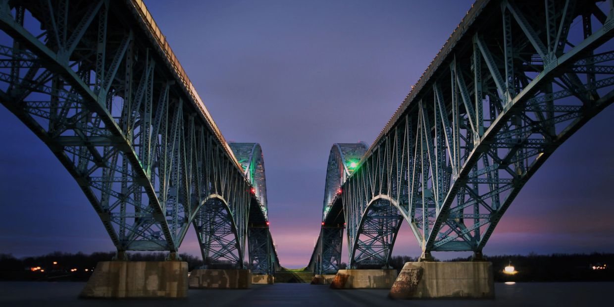 Symmetrical view of two illuminated steel bridges at dusk.
