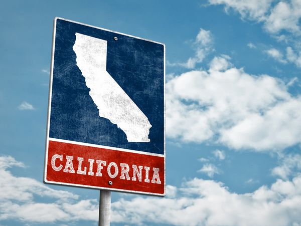 A weathered California road sign against a blue sky with clouds.
