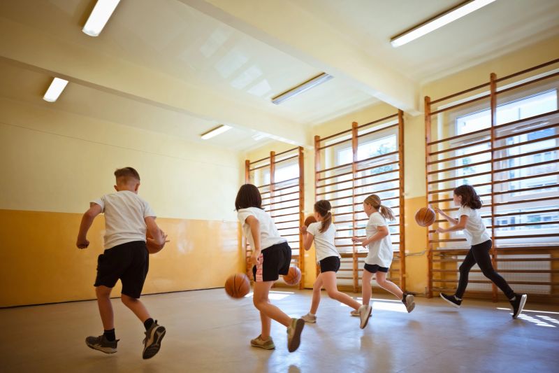 Back view of elementary school girls and boy practicing dribbling and basketball in the gym during sport lesson.