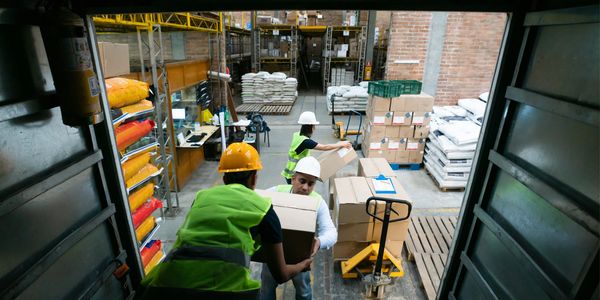 Workers in safety gear handling boxes in a busy warehouse.