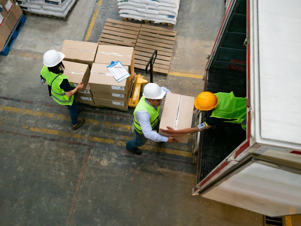 Trois travailleurs chargent des cartons dans un camion.