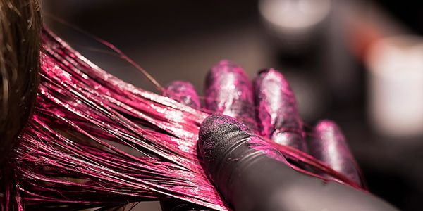 Hair being dyed purple with gloved hands applying.