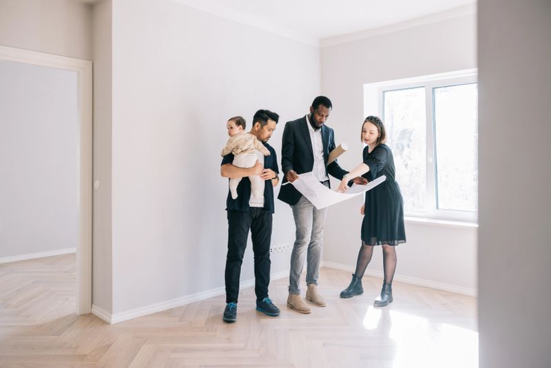 Multi-racial young family and Real Estate AGent, looking together at potential home blueprints.