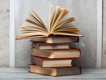 A stack of old hardcover books with one open on top.
