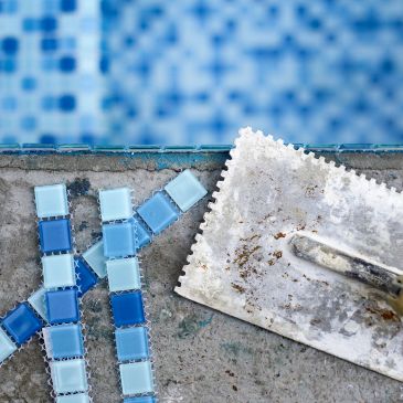 Close-up of mosaic tiles and a trowel near a pool.