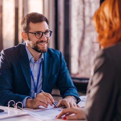 Smiling man in glasses discussing documents with a woman in a professional setting.