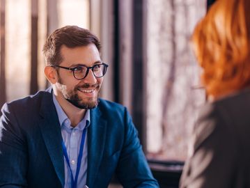 A man in glasses smiling during a conversation.