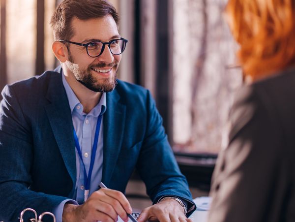 Smiling man in glasses discussing documents with a woman in a professional setting.