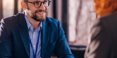 Smiling man in glasses discussing documents with a woman in a professional setting.