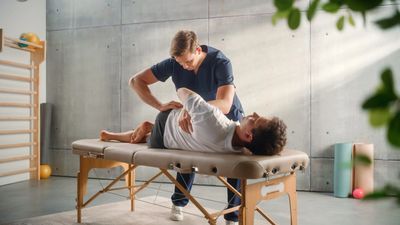 A physiotherapist treats a patient on a massage table in a modern clinic.