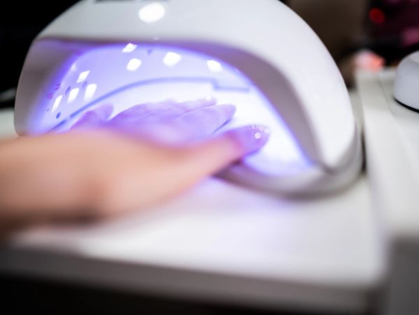 A hand under a UV nail lamp curing gel polish.