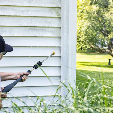 Person spraying pesticide on house siding and plants.