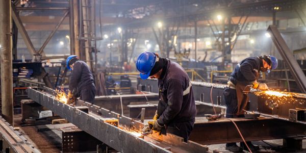 Workers grinding metal beams in a factory.