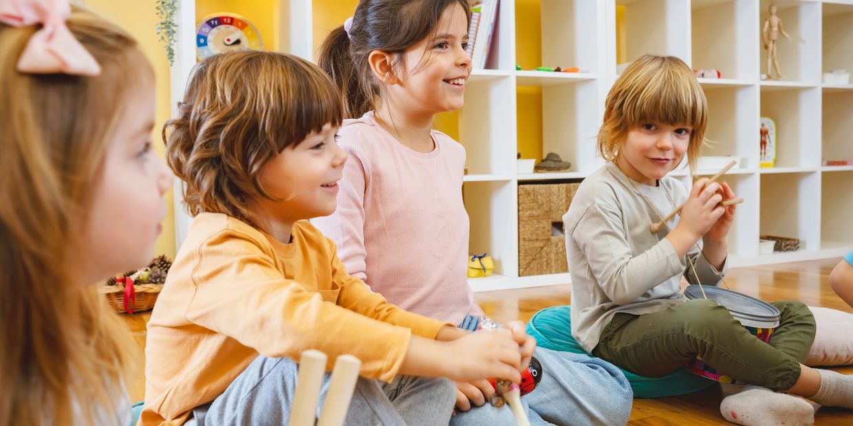 Children sitting in a circle, playing musical instruments and smiling.