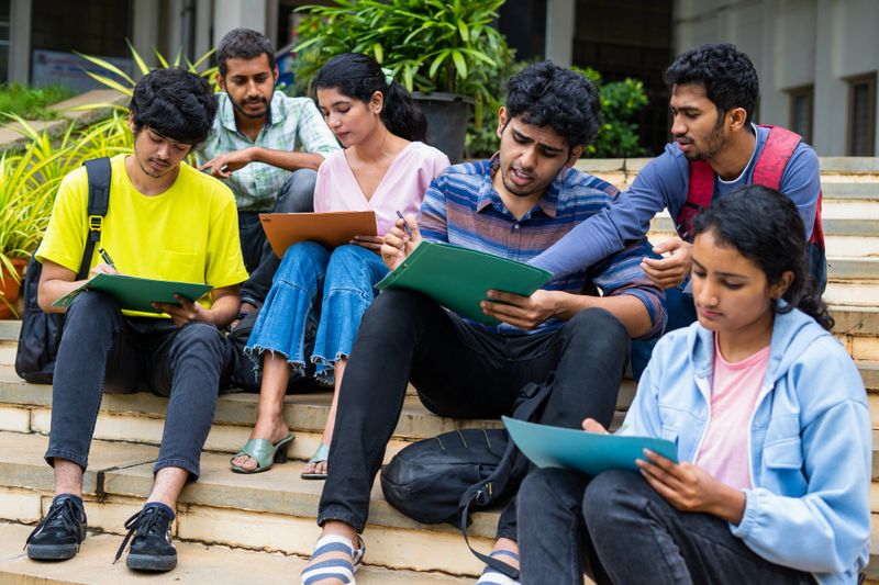 Group of students filling admission application form or preparing for exams on college campus by discussing eachother - concept of graduation, skill development and examination